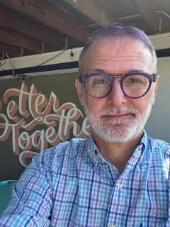 Head and Should shot of Darin with glasses, smiling in front of a sign, "Better together"